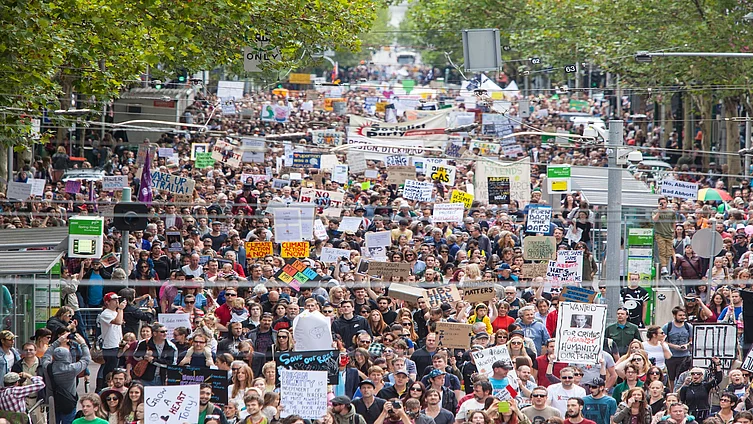 Large crowd of protesters marching down a city street in Melbourne, holding signs about climate action and social justice